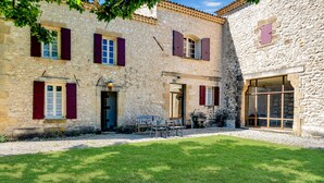A stone building with multiple windows and shutters, a grassy courtyard, and a door leading to an interior space. - Petite Bastide | Domaine Tour Campanets (Le Puy-Sainte-Réparade)