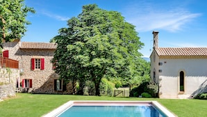 A stone house with a swimming pool, surrounded by lush greenery and a large tree. - Petite Bastide | Domaine Tour Campanets (Le Puy-Sainte-Réparade)