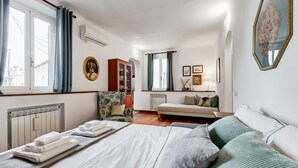 Une chambre d’hôtel comprenant un lit, un canapé, une chaise, un radiateur, une fenêtre avec des rideaux et un tableau accroché au mur.