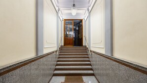 Un couloir se terminant par une porte en bois, des marches en marbre et un luminaire au plafond.