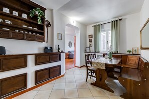 A kitchen with wooden cabinets, a dining table, and chairs. There is a plant on the cabinets and a window with curtains. - Penthouse Brancaccio - Wide Panoramic Terrace (Roma)