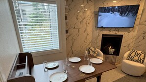 A dining area with a wooden table set for four, a fireplace, and a TV mounted on the wall. - Mountain Bluebird Condo Getaway at Schweitzer Ski Resort (Sandpoint)