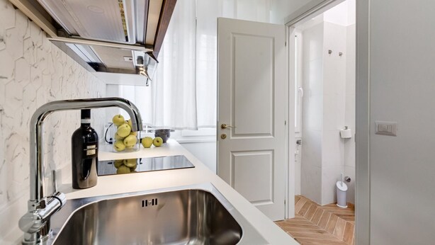 Una cocina con un lavamanos de acero inoxidable, una botella de vino y limones en la encimera.