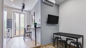 Une cuisine moderne avec un coin repas, un téléviseur fixé au mur et une porte-fenêtre coulissante donnant sur un balcon extérieur.