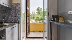 Une cuisine équipée d’un évier, de placards et d’une fenêtre donnant sur un balcon et des arbres.