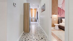 Ein Korridor mit einem gemusterten Boden, einer Holzsäule, einem Badezimmer mit Toilette und Waschbecken sowie einem Bett mit Kopfteil.