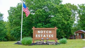 Un letrero de madera con la inscripción 'NOTCH ESTATES', rodeado de follaje y una bandera.