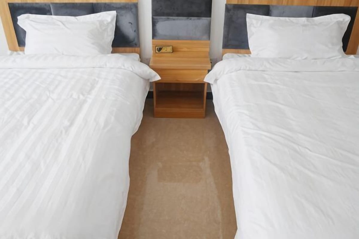 Habitación doble con dos camas, mesitas de noche de madera y un pequeño estante de madera.