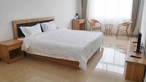 Ein ordentlich eingerichtetes Hotelzimmer mit Bett, Nachttischen, Schreibtisch, zwei Stühlen und einem Fernseher.