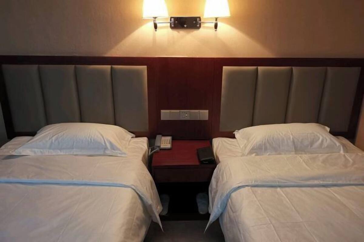 Hotellihuone, jossa on kaksi sänkyä, yöpöytä, lamppu ja seinälle asennettu puhelin.