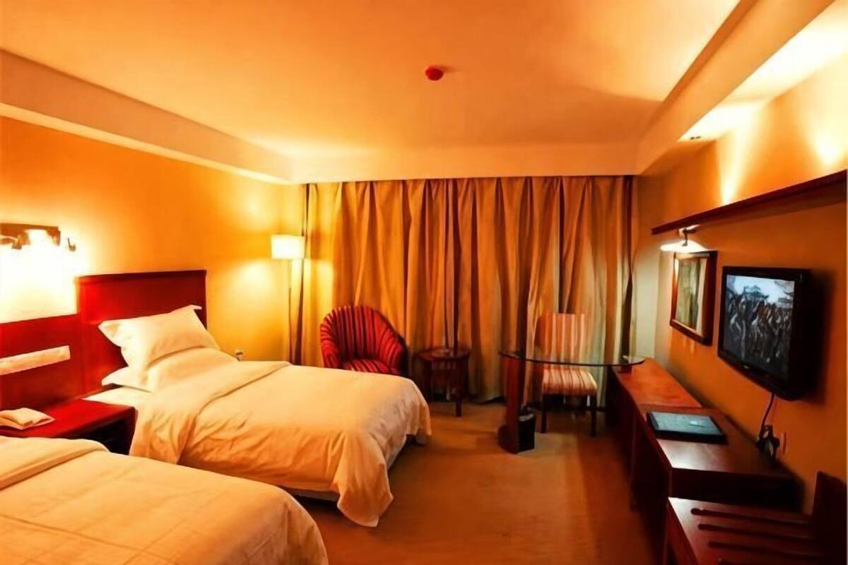 Hotellihuone, jossa on kaksi sänkyä, työpöytä, tuoli, televisio ja verho.