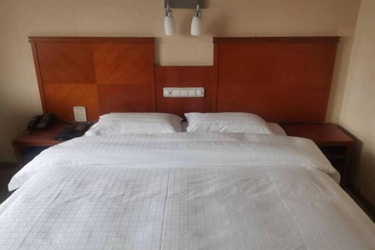 Hotellihuone, jossa on suuri sänky, kaksi yöpöytää, puinen pääty ja seinään kiinnitetty valaisin.