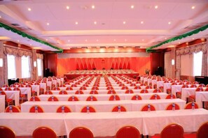 A banquet hall with rows of tables and chairs, a stage, and a presentation screen.