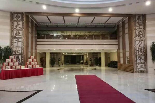 A spacious lobby with a red carpet, a reception desk, and a large chandelier.