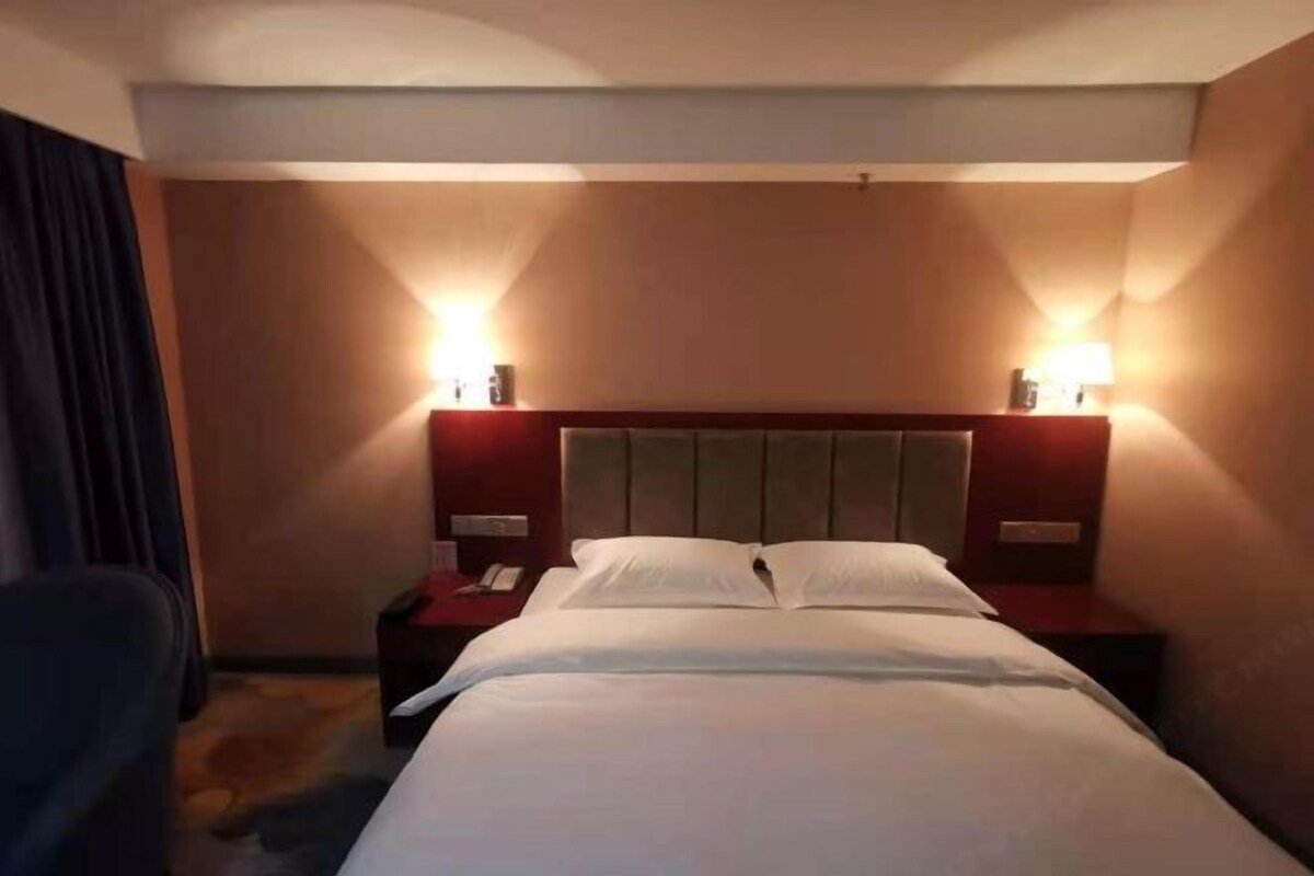 Una habitación de hotel con una cama, dos mesitas de noche con lámparas, una silla y suelo alfombrado.