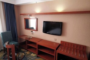 Habitación de hotel con una televisión montada en la pared, una mesita, una silla y un banco de madera.