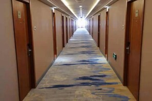 Pasillo de hotel con puertas a ambos lados, una alfombra estampada y una fuente de luz al final.