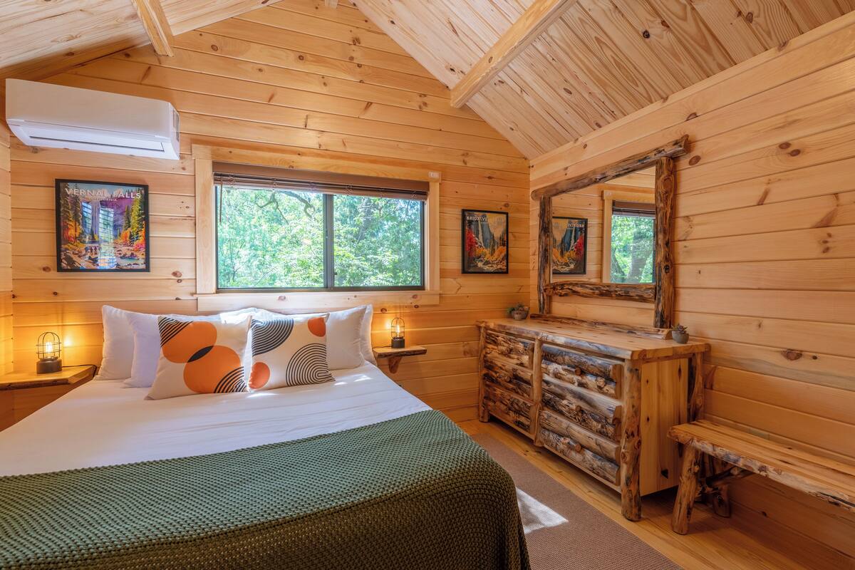 A wooden cabin bedroom with a bed, nightstands, a dresser, and a large mirror.