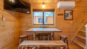 Et interiør af en træhytte med et spisebord, barstole, et fjernsyn og en aircondition.