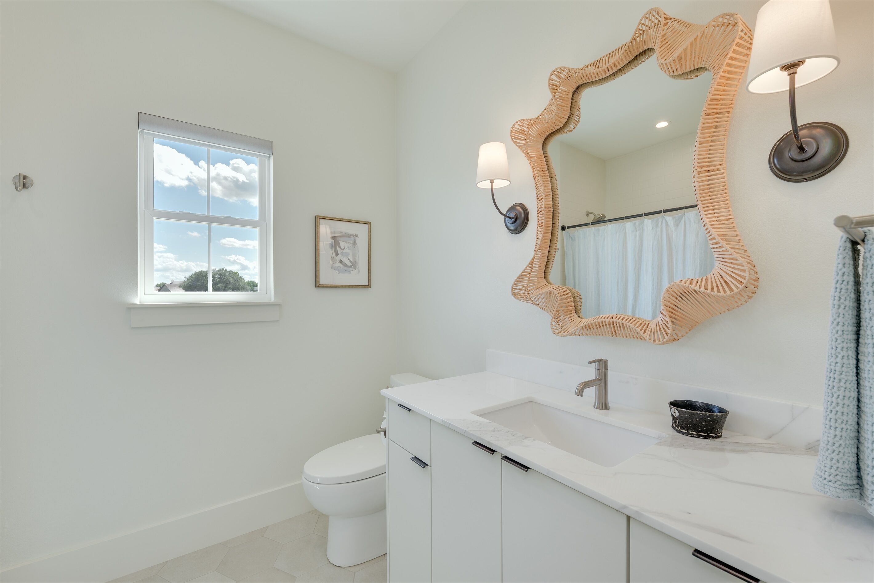 A bathroom with a white sink, a large mirror, and a window with a view of the sky.