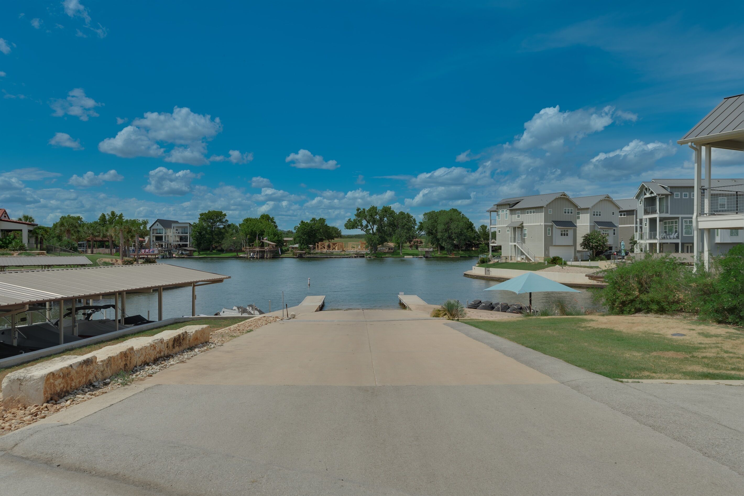 A lakeside view with a dock, a covered seating area, and residential buildings in the background.