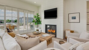 Ein modernes Wohnzimmer mit Kamin, weißen Sofas, einem Couchtisch und einem großen Fenster mit Blick auf einen Pool und Gebäude.
