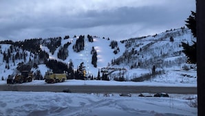 Un paysage enneigé avec une route, des véhicules utilisés pour déneiger, et une montagne en arrière-plan.