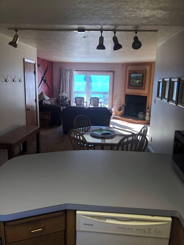 A kitchen with a built-in dishwasher, a dining area with a table and chairs, a sofa, and a fireplace.
