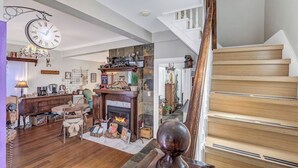 A cozy living room with a fireplace, wooden staircase, and a clock on the wall. - Downtown Rustic Luxury Garden Suite (Glenwood Springs)