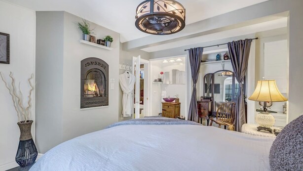 A spacious bedroom with a large bed, a fireplace, a mirror, and a view into the bathroom. - Downtown Rustic Luxury Garden Suite (Glenwood Springs)
