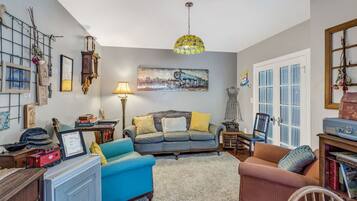 A cozy living room with a blue sofa, a red armchair, and a coffee table. There is a painting on the wall, a lamp, and a bookshelf.