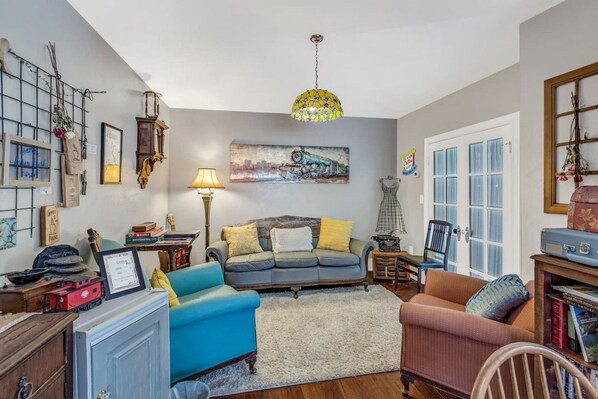 A cozy living room with a blue sofa, a red armchair, and a coffee table. There is a painting on the wall, a lamp, and a bookshelf.