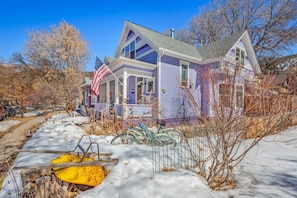 Una casa de dos pisos con un porche, una bandera y un patio cubierto de nieve.