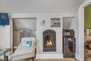 A cozy living room with a fireplace, a sofa, a television, and a refrigerator.