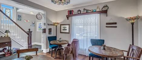 A dining area with wooden tables and chairs, a chandelier, and a staircase leading to another level.