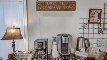 Een koffiehoek met een koffiezetapparaat, kopjes en een bordje met de tekst 'Ik zou koffie opgeven, maar ik ben geen bladverliezer.'
