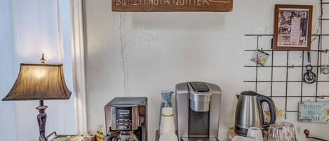 A coffee station with a coffee maker, cups, and a sign saying 'I'D GIVE UP COFFEE, BUT I'M NOT A QUITTER.'