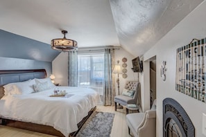 A bedroom with a bed, bedside table, lamp, chair, and decorative wall art.
