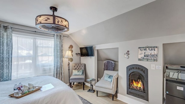 A modern bedroom with a bed, a fireplace, a TV, and a dining area with a tray of water bottles.
