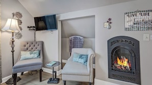 A cozy living room with two upholstered chairs, a fireplace, a television mounted on the wall, and a small side table.