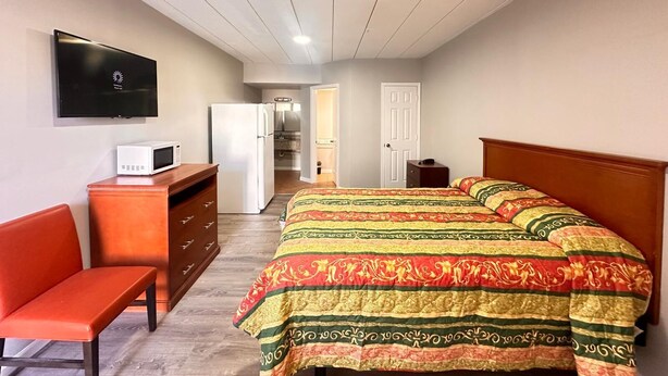A bedroom with a bed, a desk, a chair, a TV, and a refrigerator.
