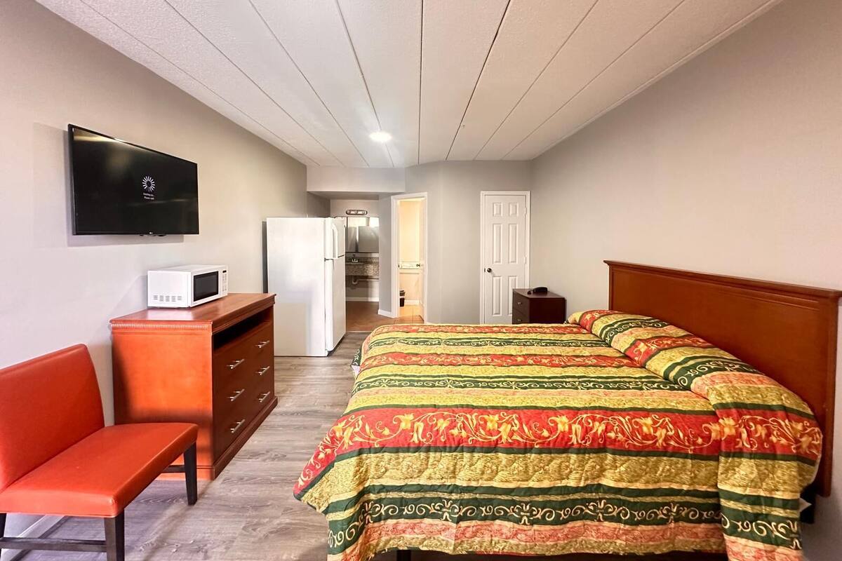 A bedroom with a bed, a desk, a chair, a TV, and a refrigerator.