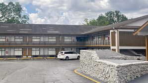 A motel with a parking lot, a white car parked, and a stone wall in the foreground.