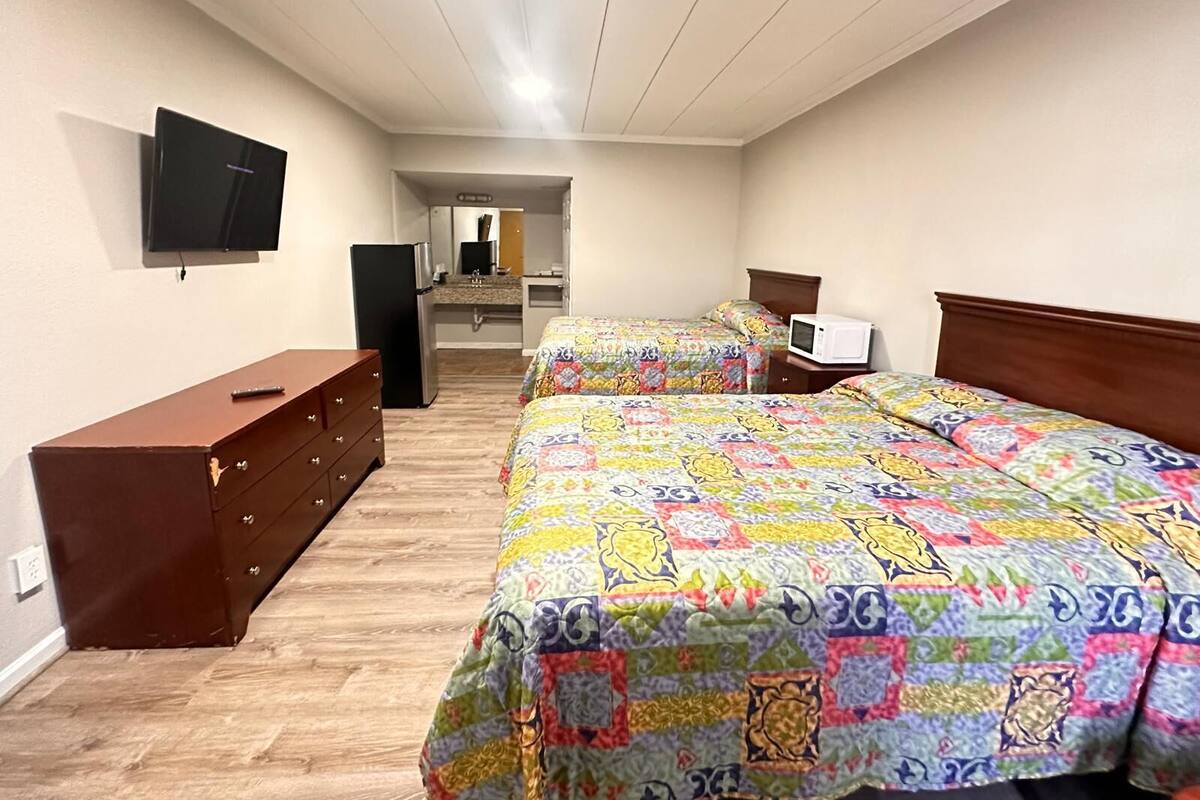 A bedroom with two beds, a dresser, a TV, and a microwave.