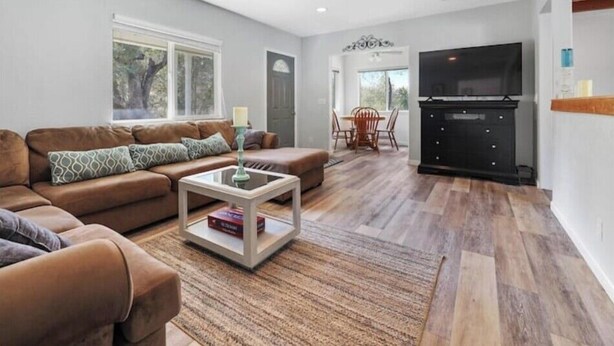 A modern living room with a brown leather sofa, a glass coffee table, and a dining area with a wooden table and chairs. - A cozy cottage in Sequoia area! (Three Rivers)