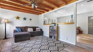 A modern living room with a grey sofa, patterned rug, ceiling fan, bookshelf, and wooden flooring. - A cozy cottage in Sequoia area! (Three Rivers)