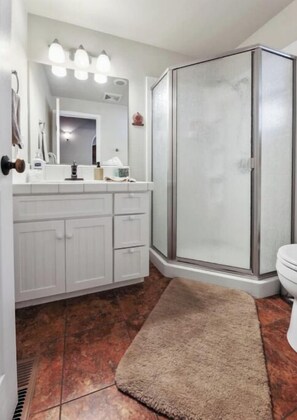Une salle de bain avec un meuble-lavabo blanc, une cabine de douche en verre et un tapis marron sur le sol.