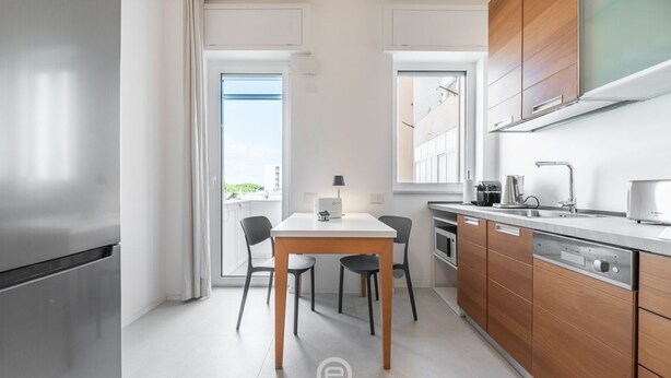 Une cuisine moderne dotée d’un réfrigérateur en acier inoxydable, de meubles en bois, d’un plan de travail blanc et d’un coin repas avec une table et des chaises.