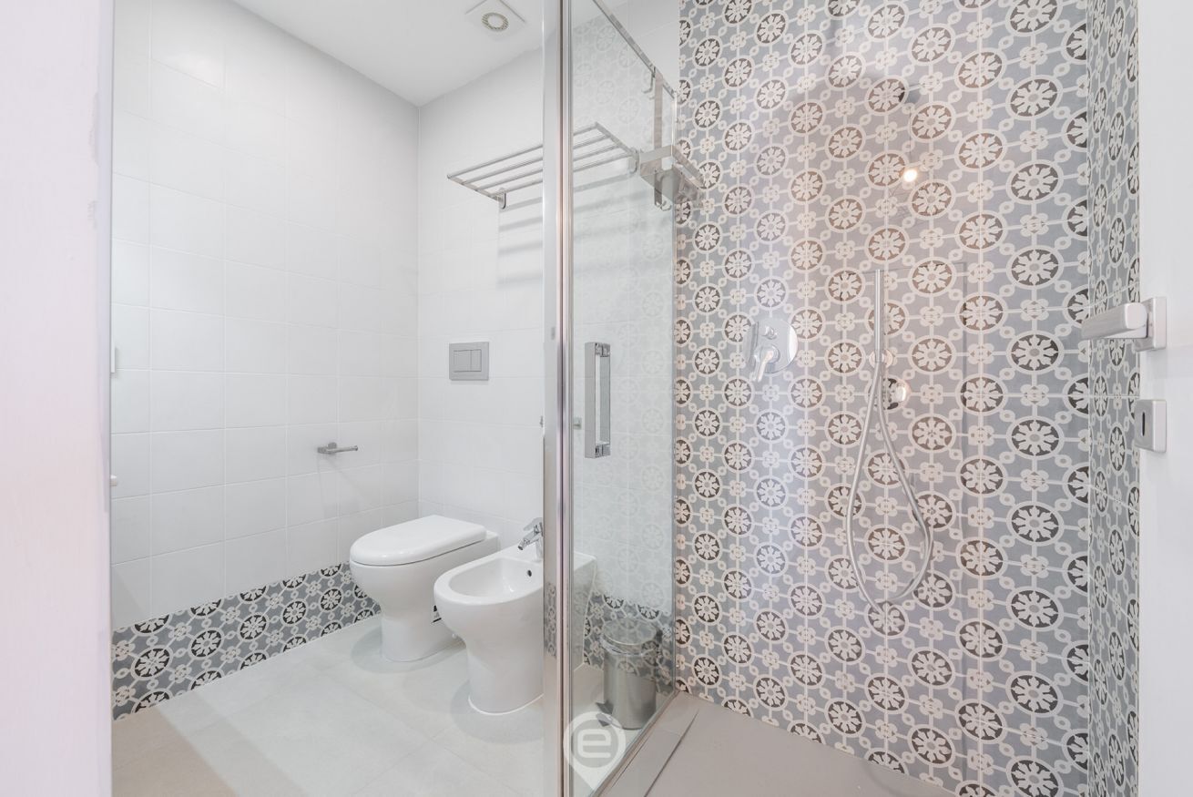 A modern bathroom with a glass shower enclosure, a toilet, and a bidet.