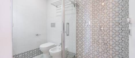 A modern bathroom with a glass shower enclosure, a toilet, and a bidet.